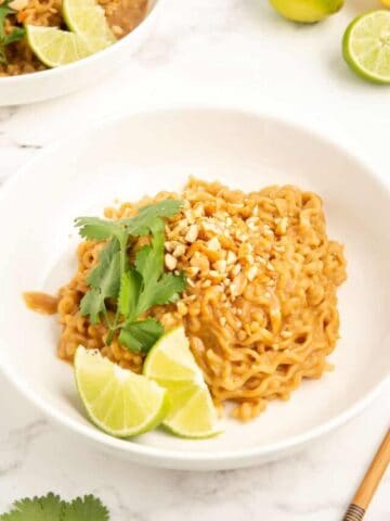 Peanut butter ramen served in a white bowl with lime wedges and cilantro.
