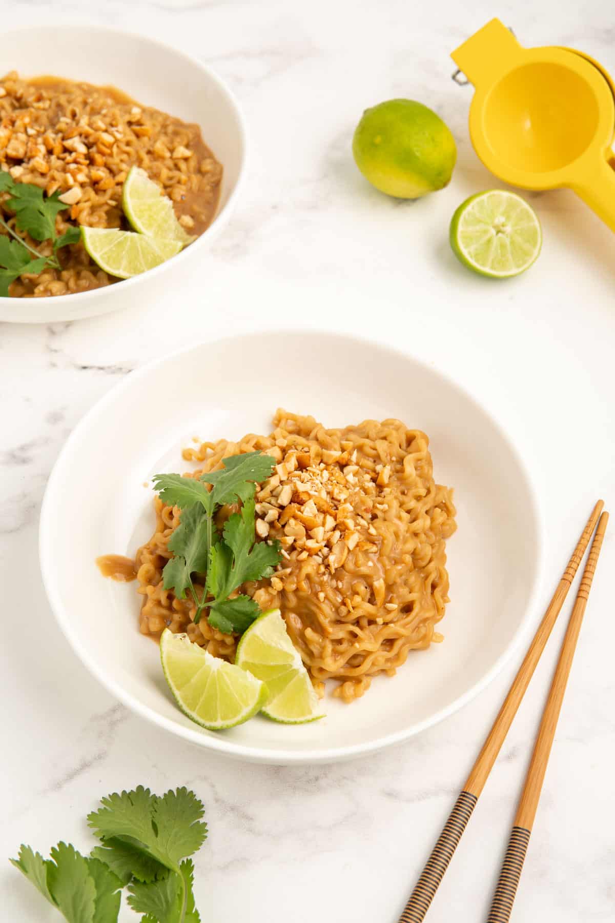 Peanut butter ramen served in a white bowl with cilantro and lime wedges.