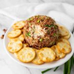 Pecan bacon cheese ball on a cake stand with crackers and green onions.