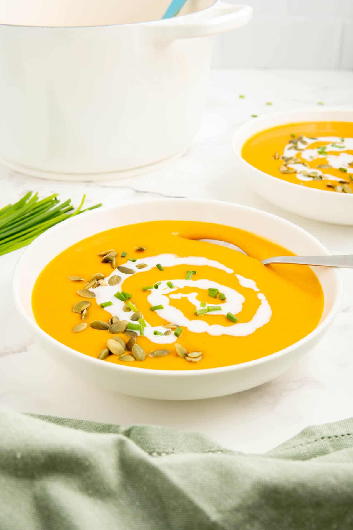 A bowl of pumpkin soup with coconut milk, chives, and pepitas on top and a spoon.