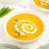 A bowl of roasted pumpkin soup without cream served with coconut milk, chives, and pepitas.