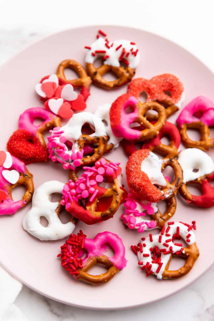 An assortment of Valentines chocolate covered pretzels on a pink plate.