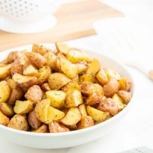 Air fryer diced potatoes in a white bowl with a spatula in the background.