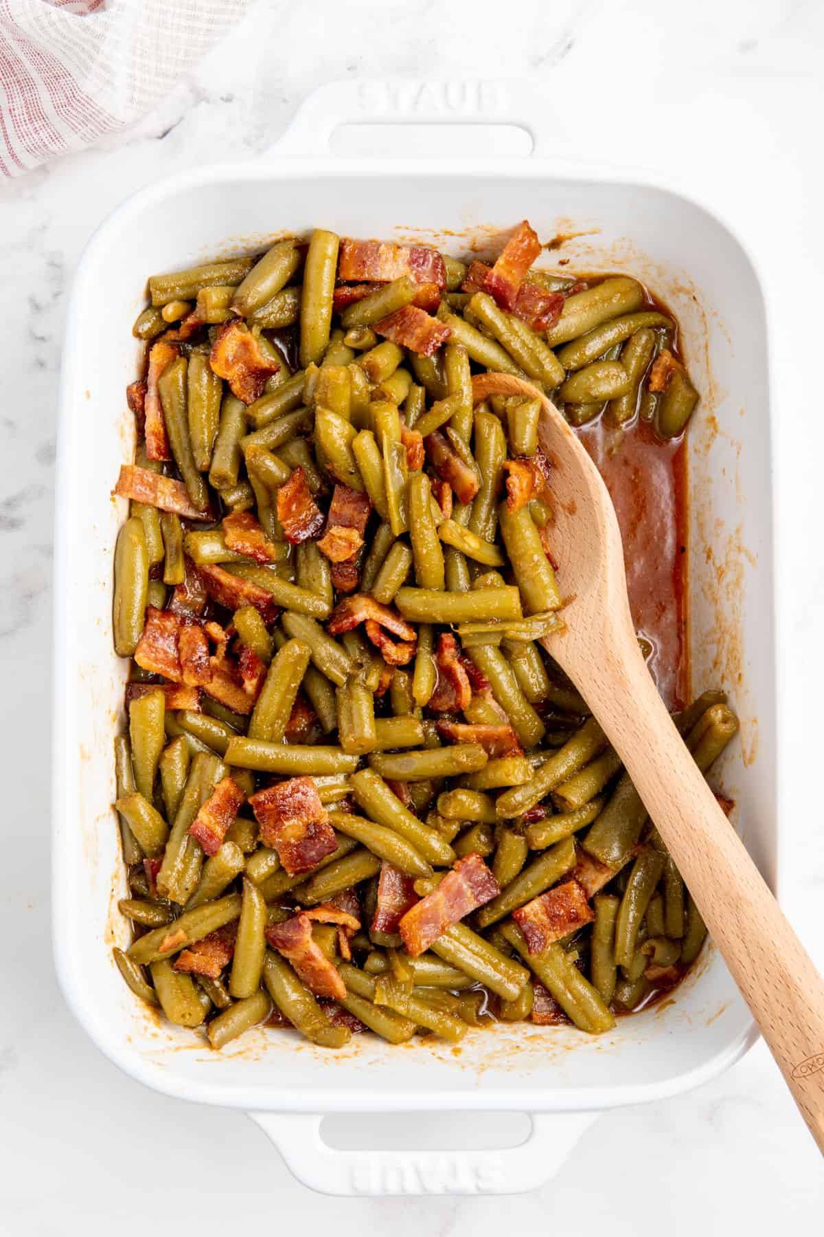 Crack green beans in a white baking dish with a wooden spoon.