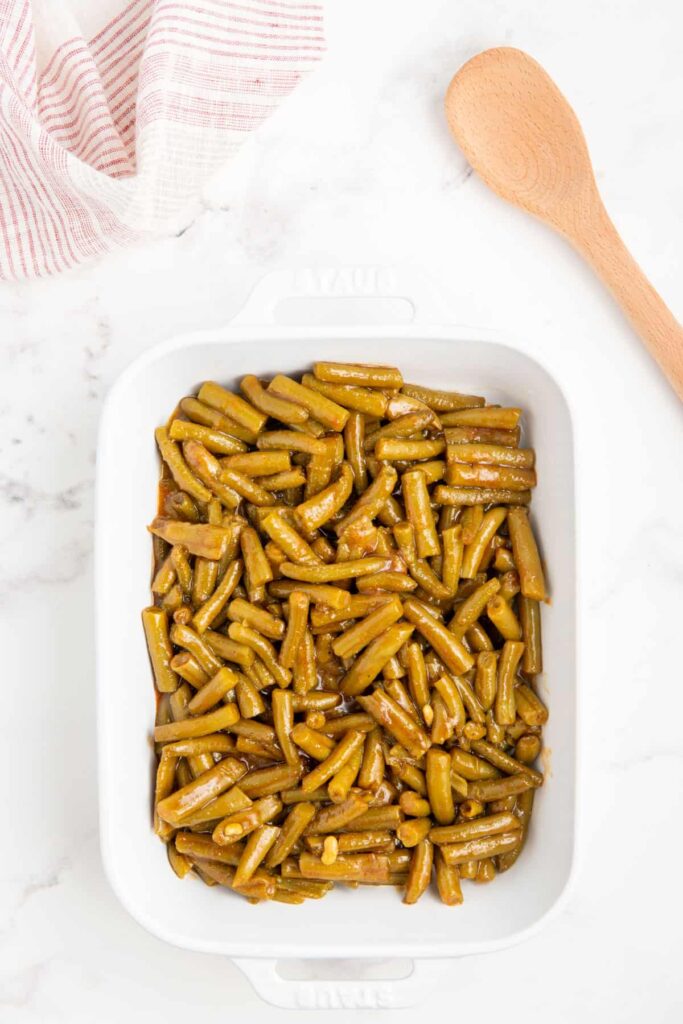 Crack green beans in a white baking dish.