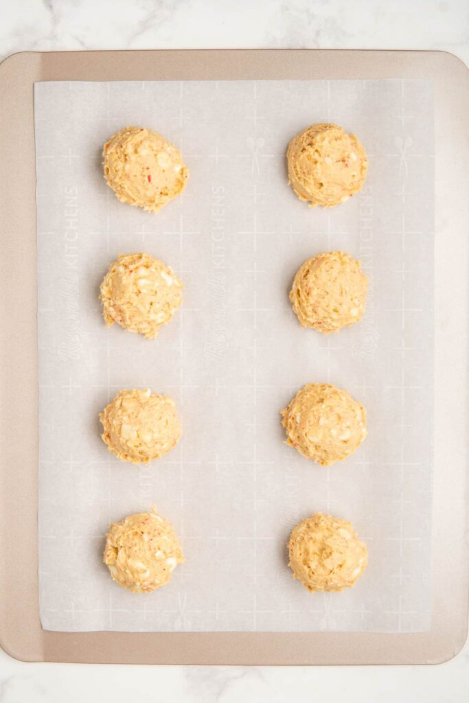 Balls of white chocolate and peppermint cookie dough on a cookie sheet.