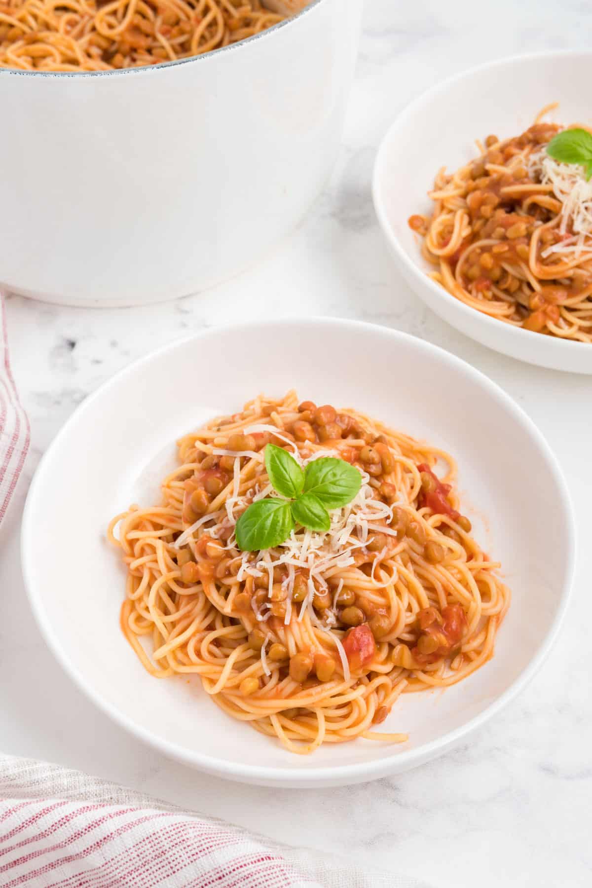 A bowl of creamy tomato lentil spaghetti with parmesan and basil.