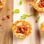 Bacon and cheese phyllo cups on a wooden board with green onions.