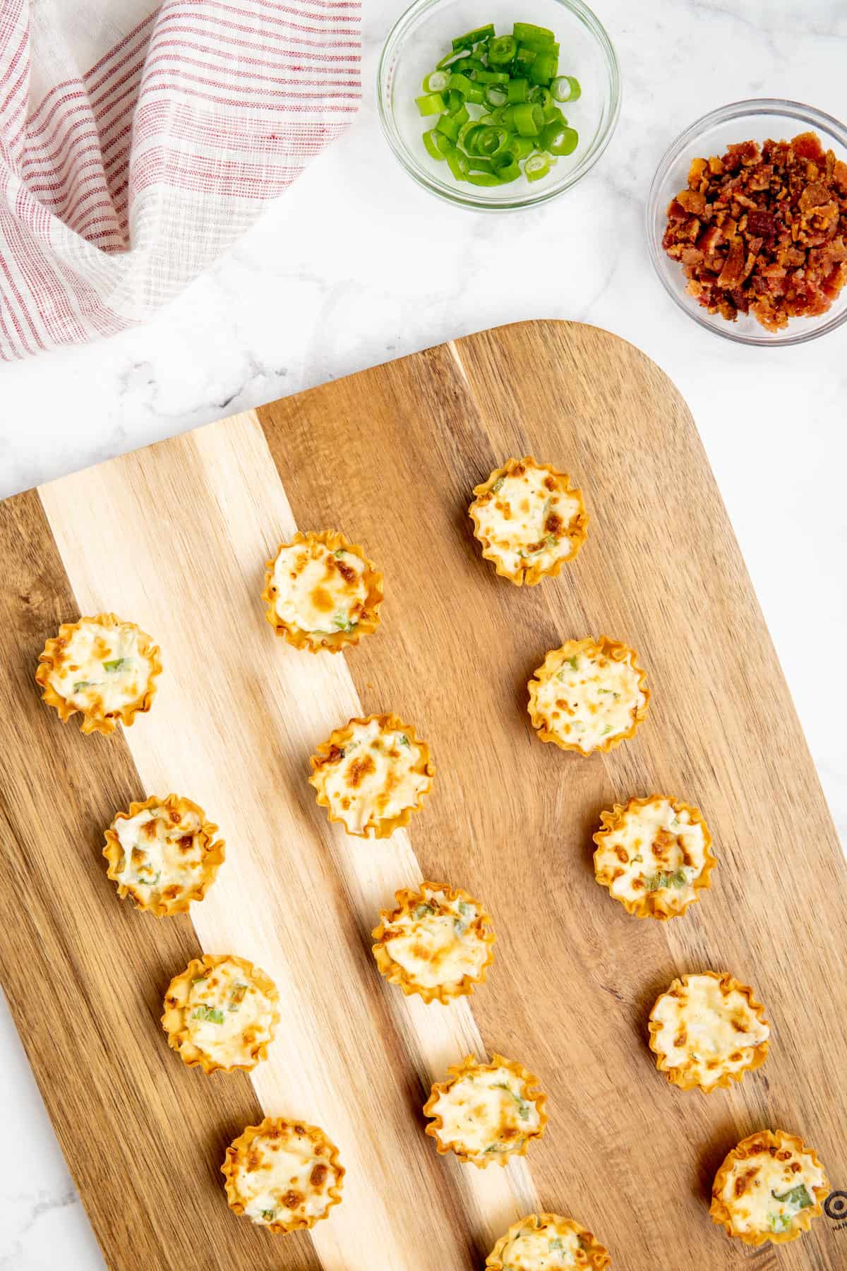 Cooked bacon and cheese phyllo cups on a board.