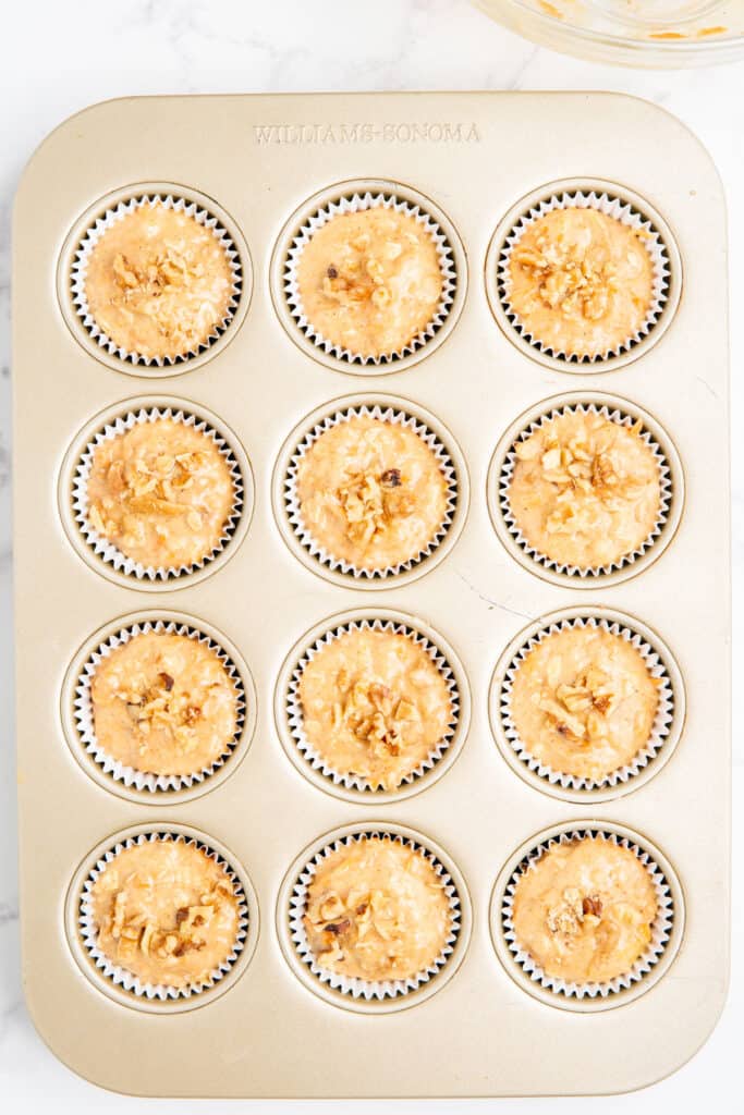 Muffin batter added to paper liners in a muffin tin with chopped walnuts on top.