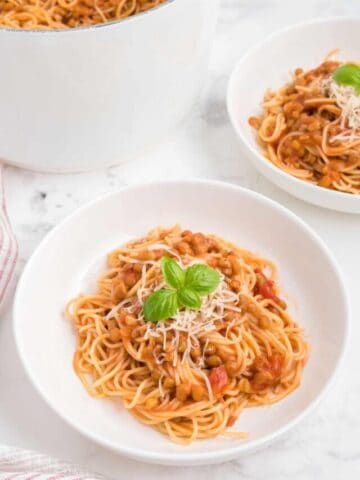 A bowl of creamy tomato lentil spaghetti with parmesan and basil.