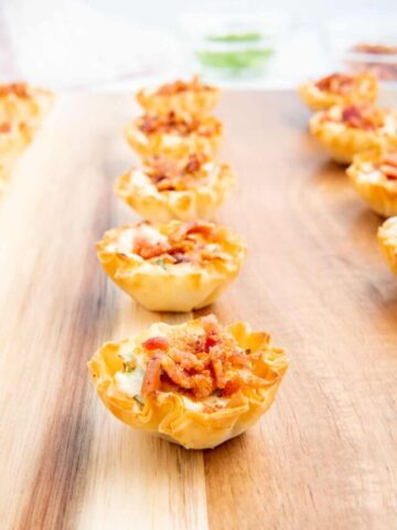 Rows of bacon and cheese phyllo cups on a wooden board.