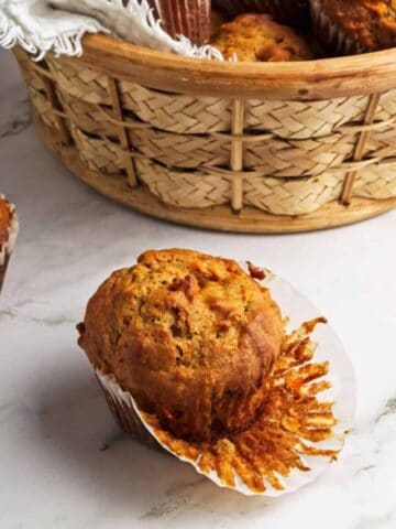 An oatmeal carrot muffin with the wrapped peeled back in front of a basket of muffins.