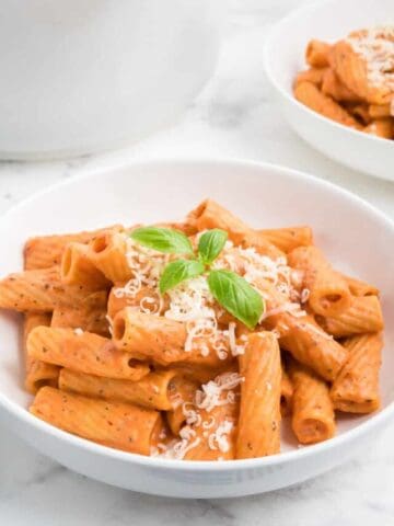 Pink sauce pasta with fresh basil and parmesan cheese in a white bowl.