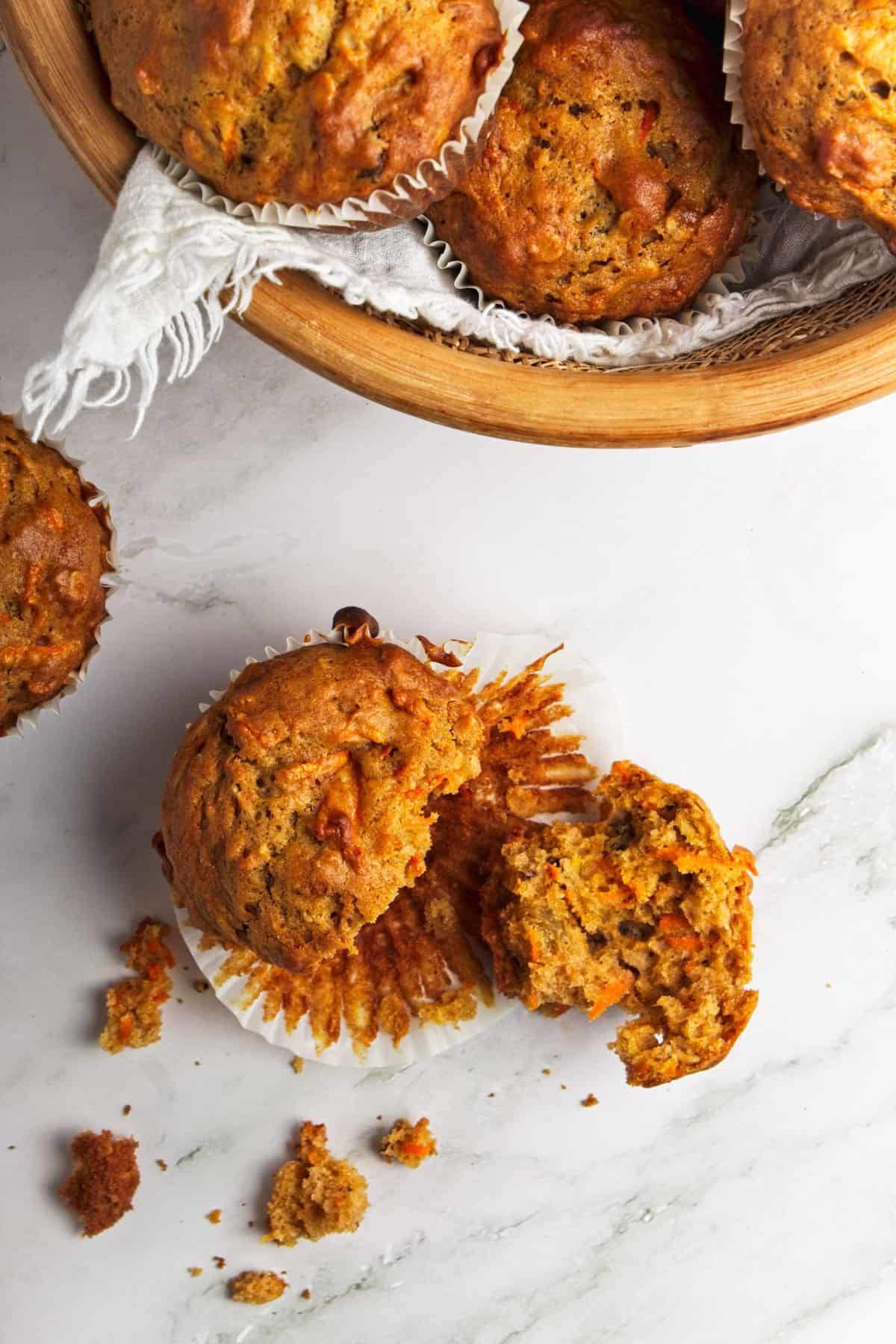 A single oatmeal carrot muffin pulled apart on a marble tabletop.