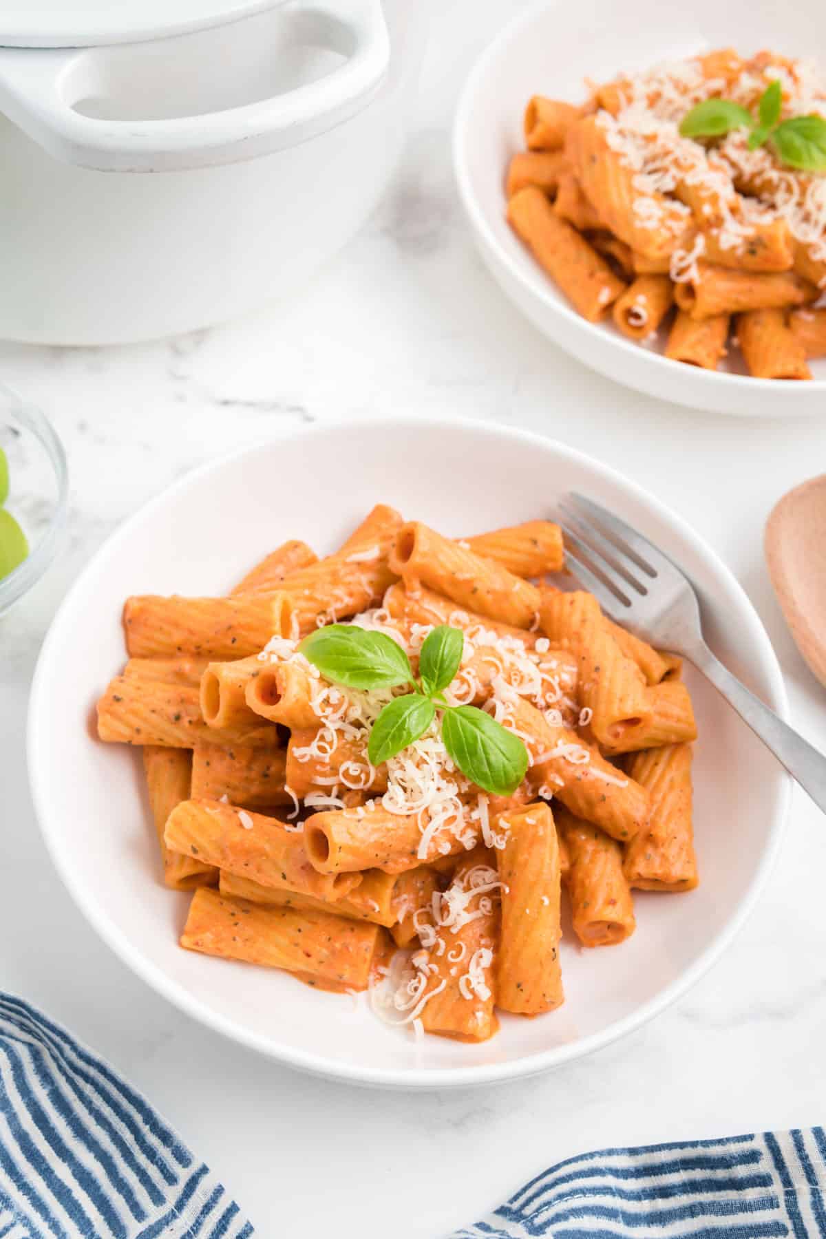 Pink sauce pasta made with Boursin cheese served in a white bowl with parmesan and fresh basil leaves.
