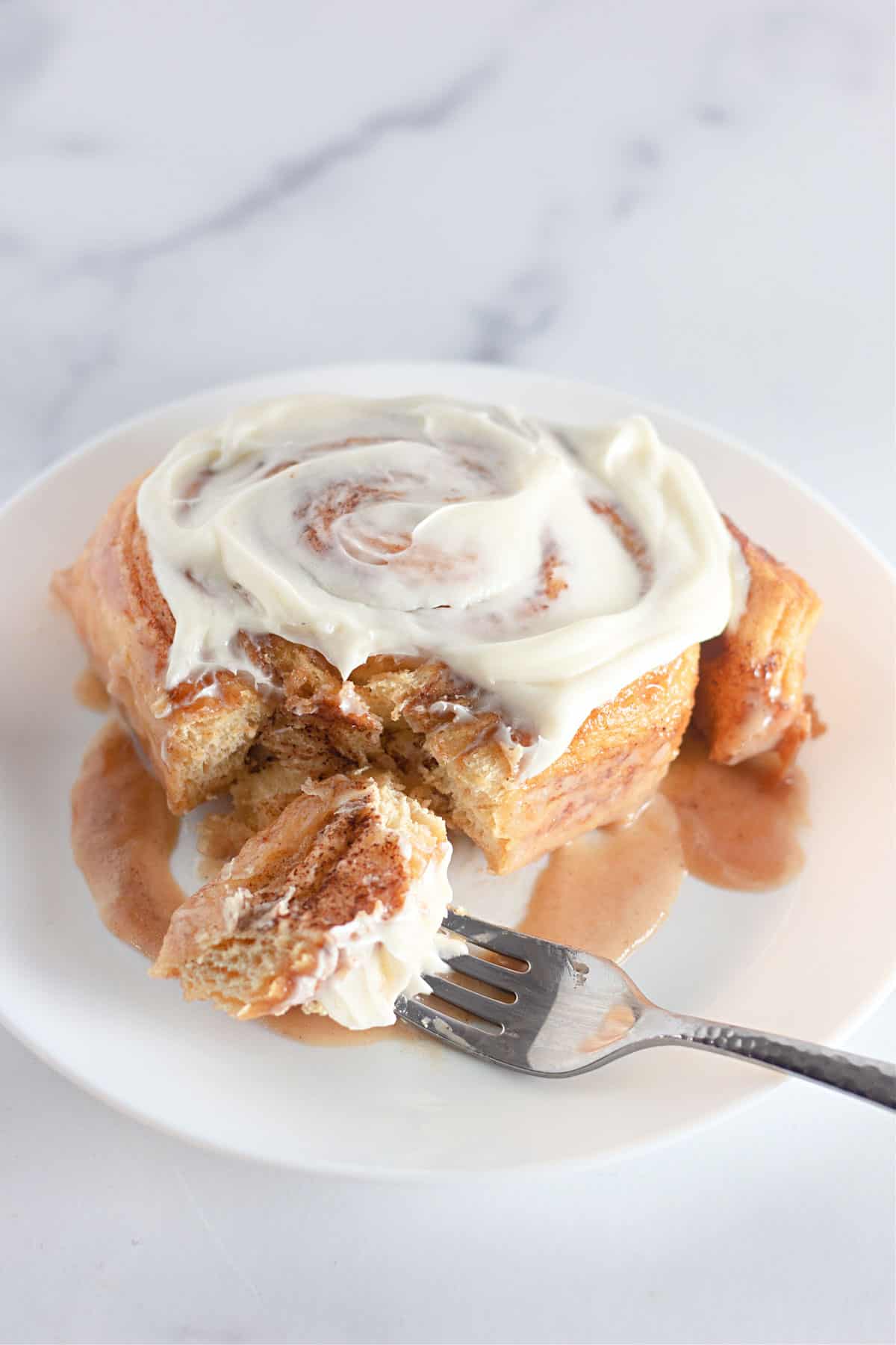A TikTok cinnamon roll with frosting on a white plate with a fork.