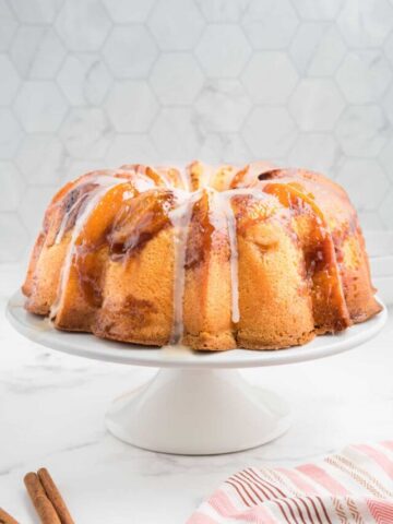 Peach cobbler pound cake with vanilla glaze on a white cake stand.