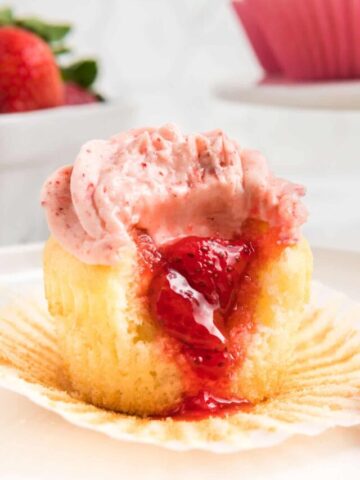 A close up of a strawberry filled cupcake with a bite taken out.