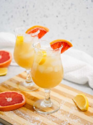 Two glasses of grapefruit tequila punch of a wooden board.