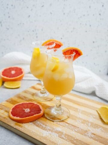 Two glasses of tequila punch garnished with grapefruit slices on a wooden board.