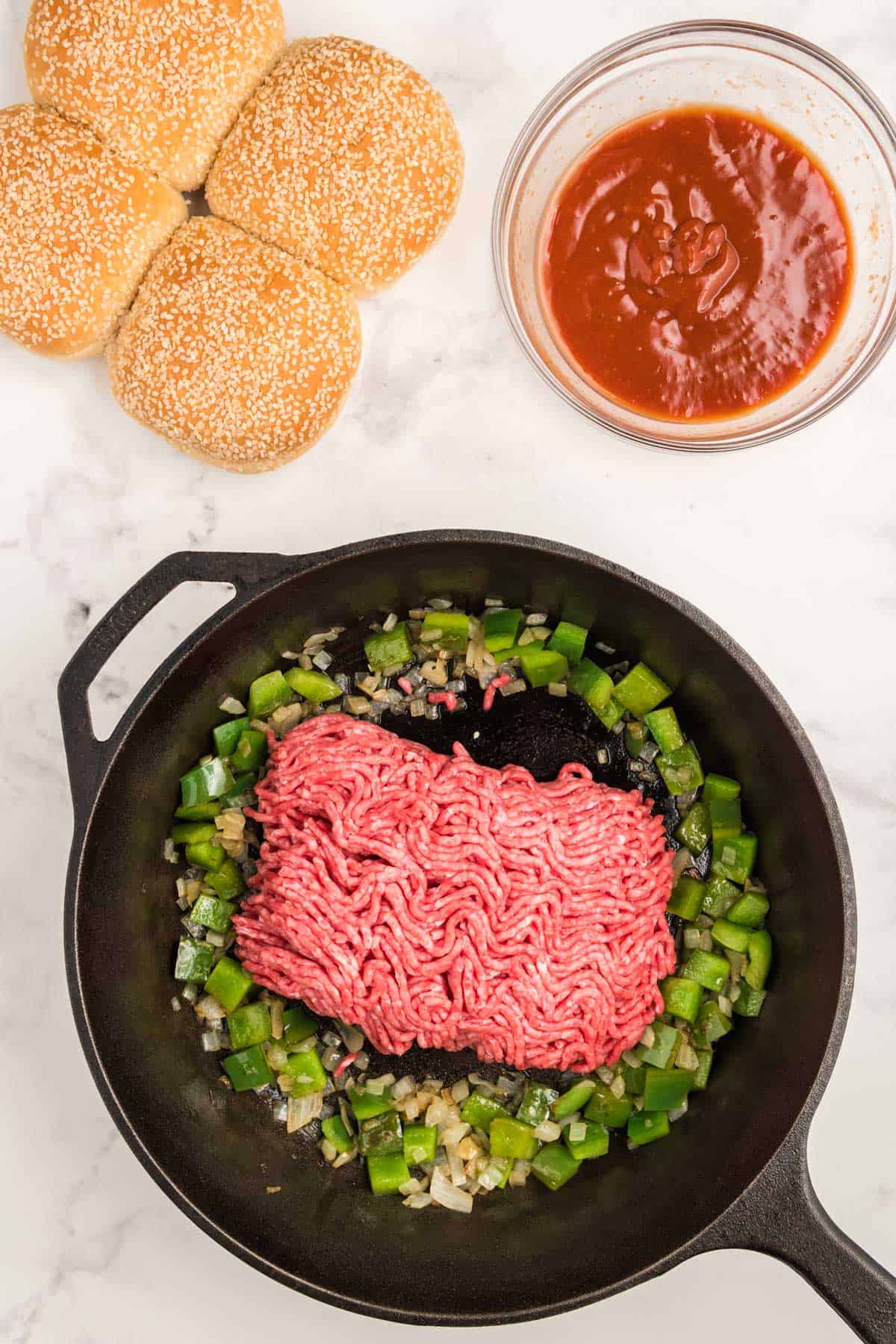 Adding ground beef to onions and green bell pepper in a cast iron skillet.