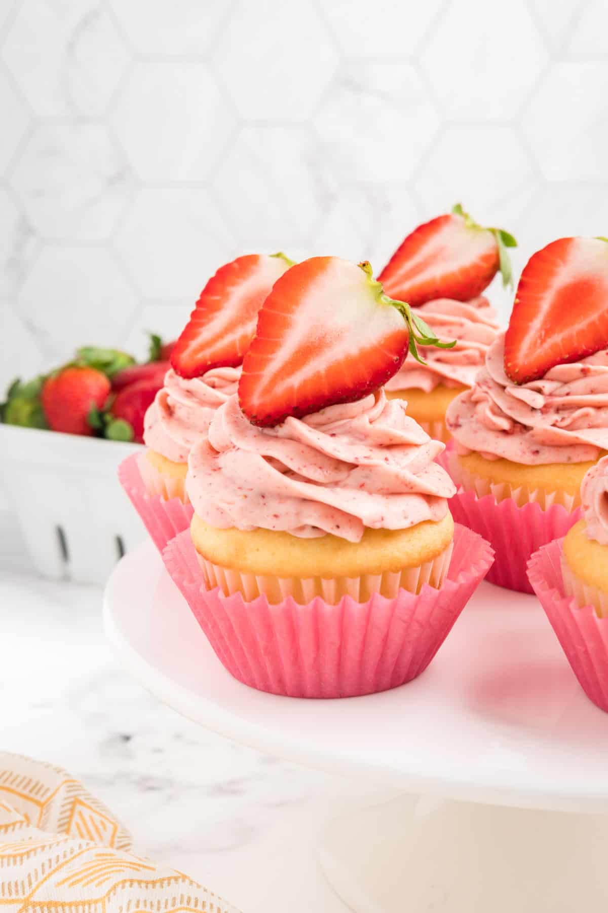 Strawberry filled cupcakes topped with fresh strawberries on a cake stand.