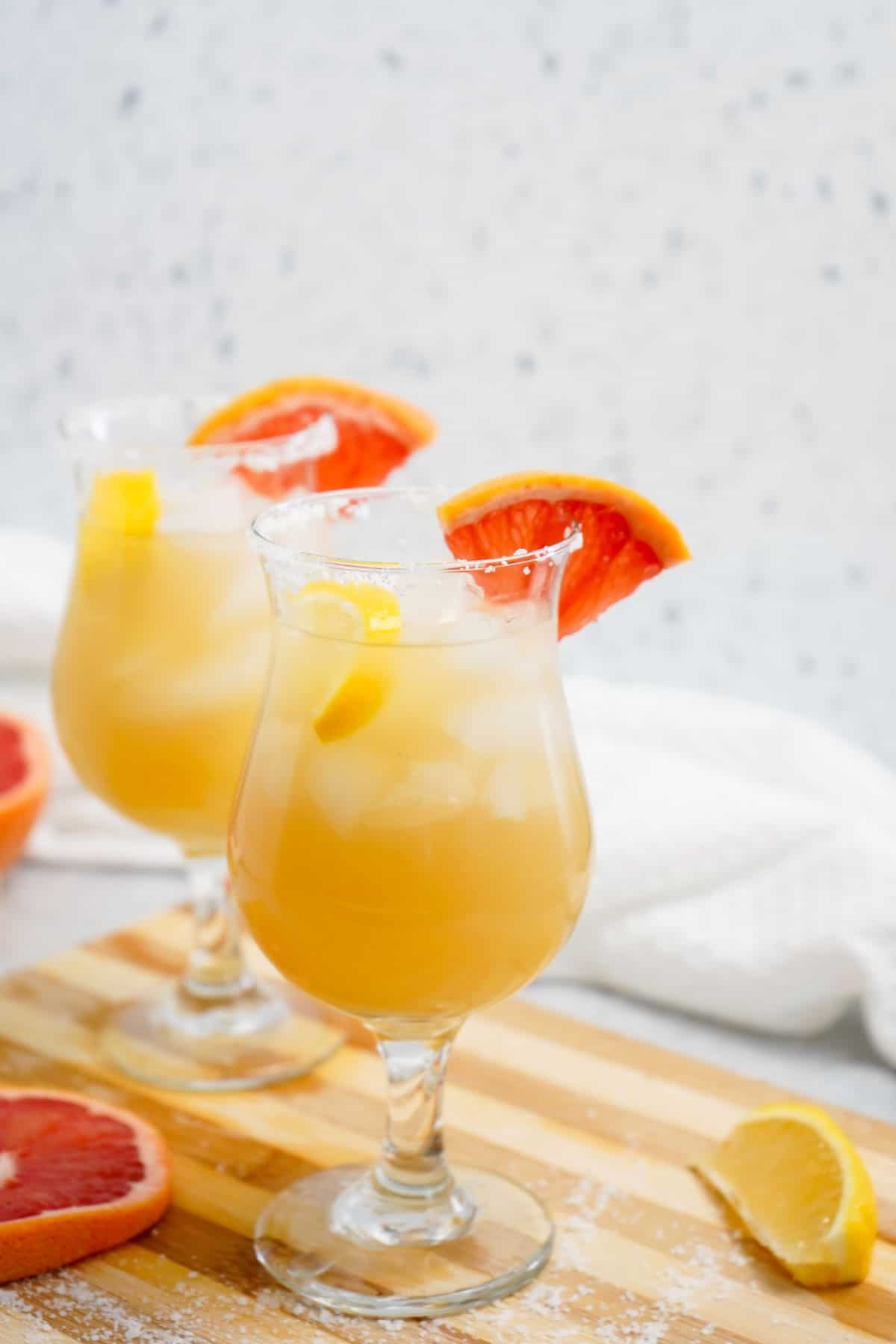 Two glasses of grapefruit tequila punch on a wooden board with salt and lemon.