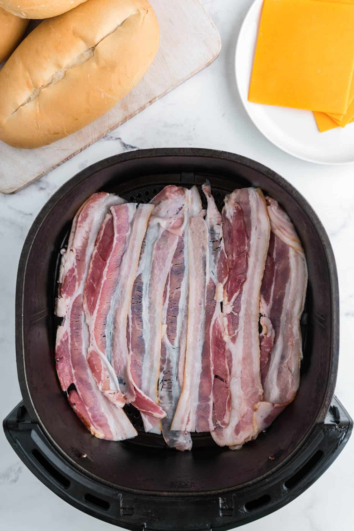 Uncooked bacon in an air fryer basket.