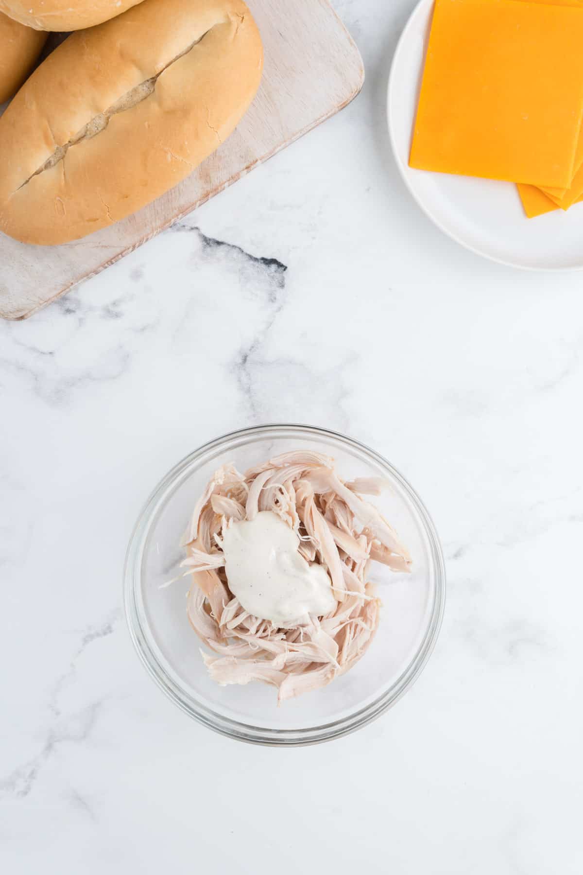 Shredded chicken in a glass bowl with a dollop of ranch dressing on top.