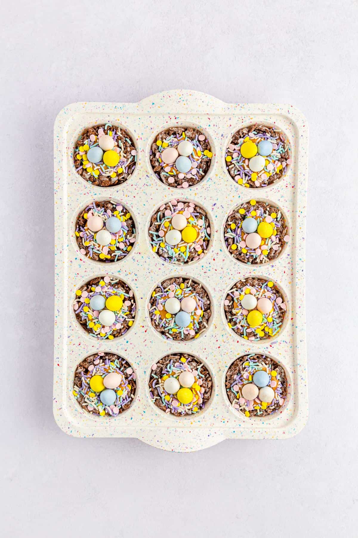 Chocolate nests topped with sprinkles and Cadbury mini eggs in a muffin pan.