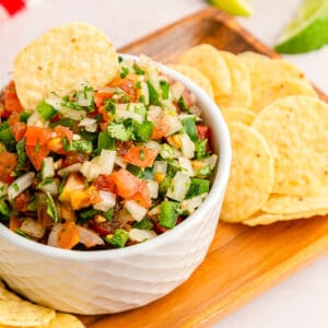 A tortilla chip dipped in classic pico de gallo with more tortilla chips on the side.