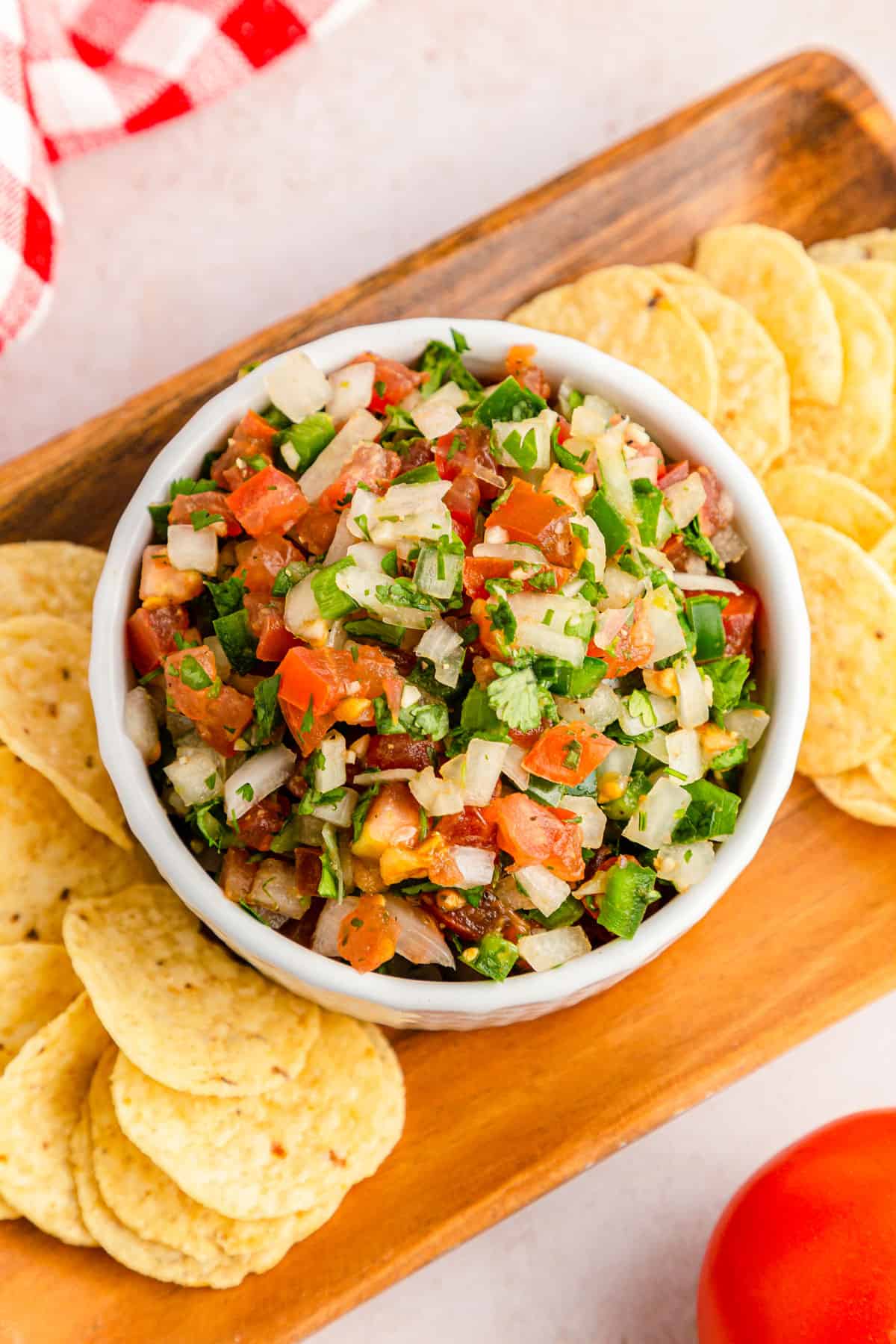 A close up overhead shot of classic pico de gallo served in a white bowl with chips.