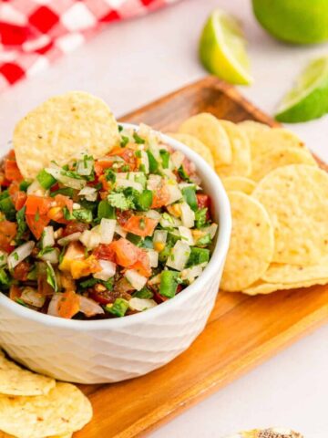 A tortilla chip dipped in classic pico de gallo with more tortilla chips on the side.