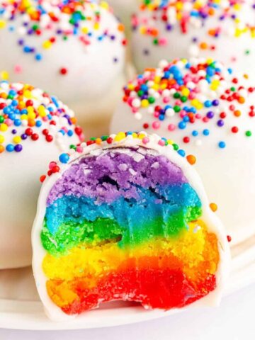 A close up shot of a rainbow cake ball with a bite taken out.