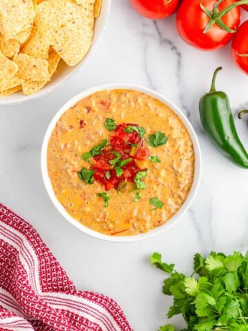 Sausage rotel dip served in a white bowl with cilantro, tomatoes, and tortilla chips.