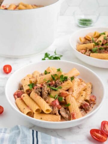 A bowl of one pot spicy sausage pasta with tomatoes and parsley.