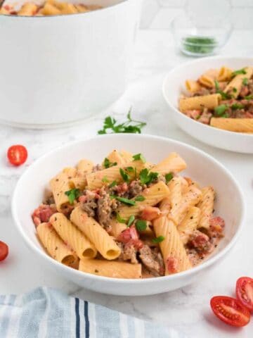 A bowl of one pot spicy sausage pasta with tomatoes and parsley.