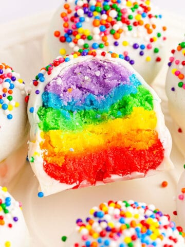 Rainbow cake balls on a plate with one ball missing a bite.