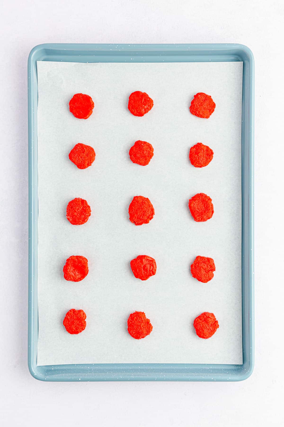 Discs of red cake ball dough on a baking tray, ready to be layered with other colors.