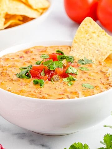 Sausage rotel dip topped with tomatoes and cilantro and served with tortilla chips.