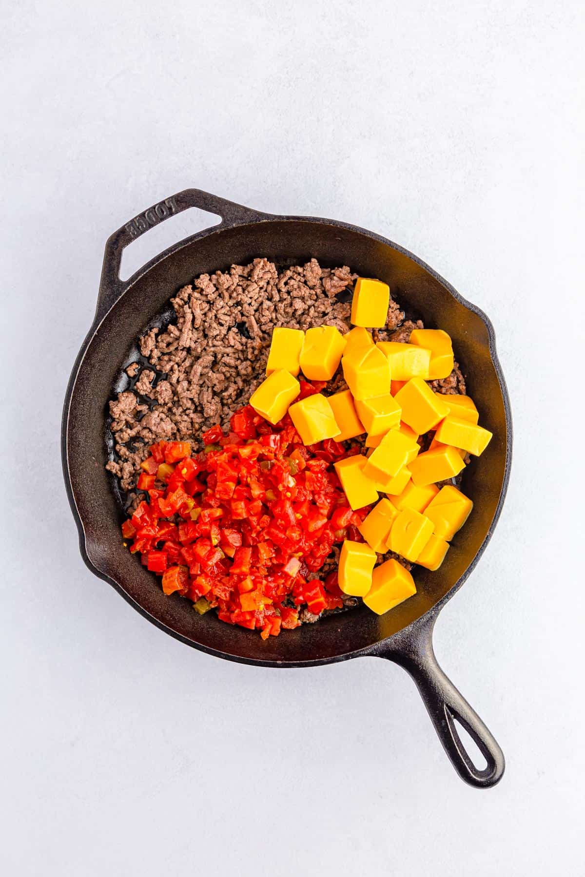 Adding Velveeta cheese and rotel tomatoes to ground beef in a cast iron pan.