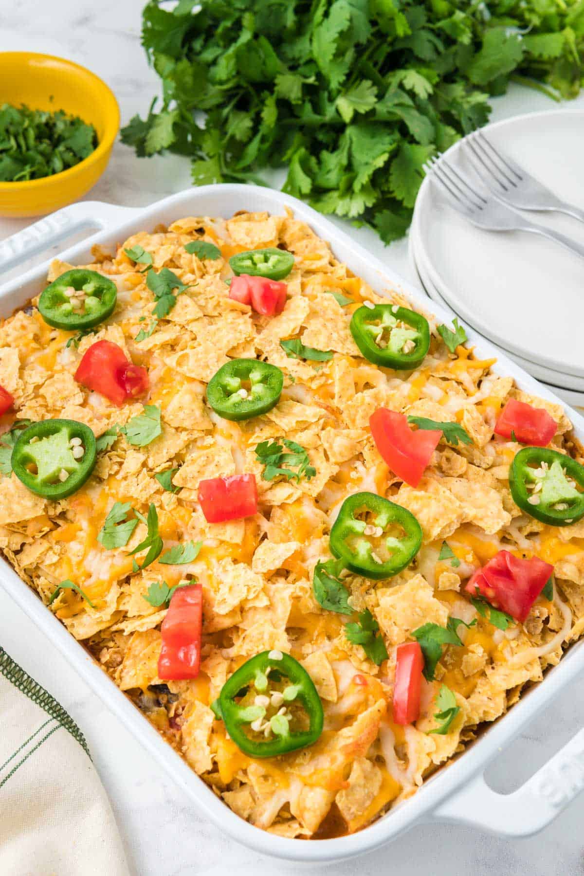 Chicken taco casserole in a white casserole dish with jalapeno slices and tomatoes on top.