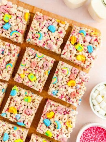 Lucky charms treats topped with sprinkles and cut into squares on a wooden board.