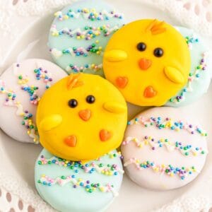 Two chick-themed chocolate covered oreos sitting on top of blue and pink Easter egg-themed oreos.