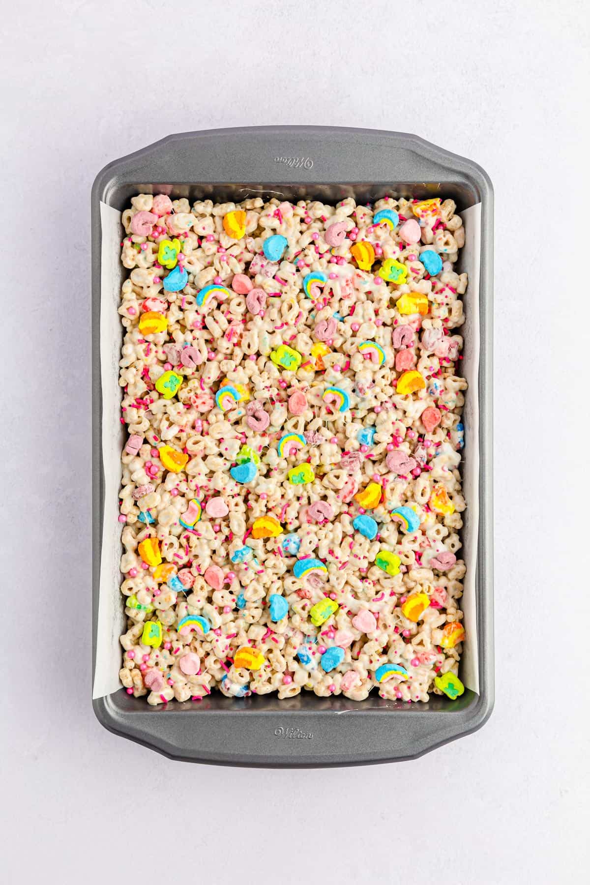 Pink sprinkles on lucky charms treats in a baking pan.