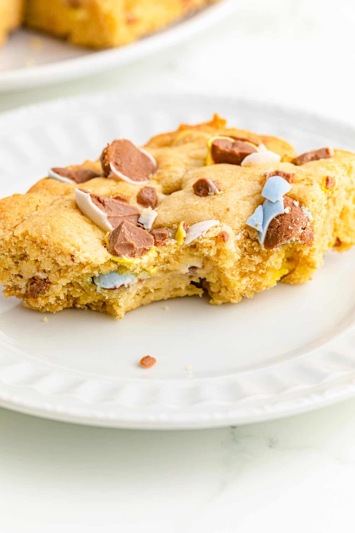 A mini egg cookie bar on a plate with a bite taken out.