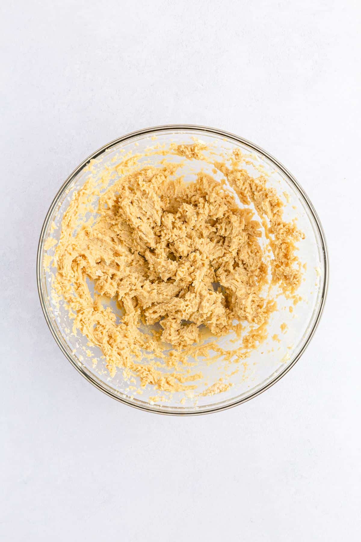 Butter and two types of sugar creamed together in a glass mixing bowl.