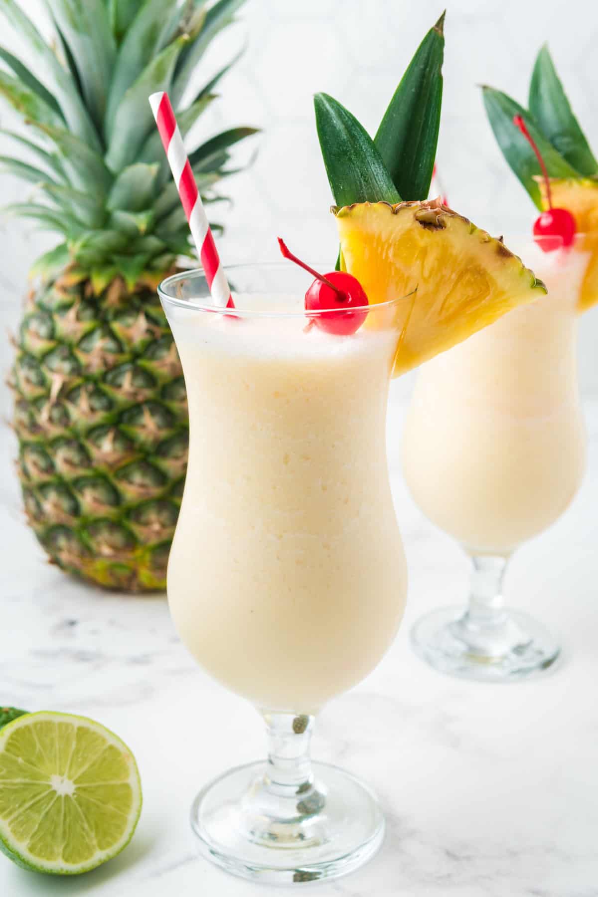 Two pina colada mocktails with a fresh pineapple in the background.