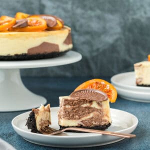 A slice of marbled chocolate orange cheesecake on a white plate with a fork.